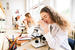 girl in white lab coat in classroom looking through microscope