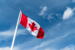Blue sky with Canadian Flag flying from pole 