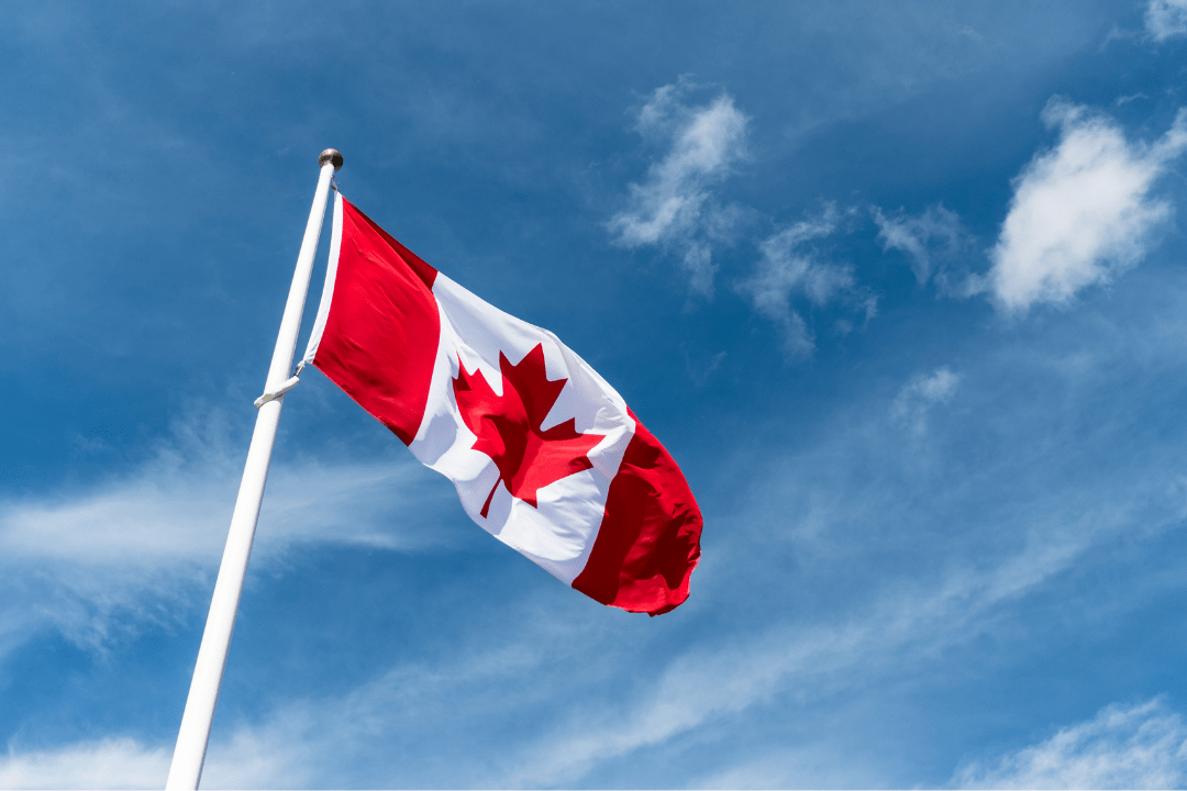 Blue sky with Canadian Flag flying from pole 