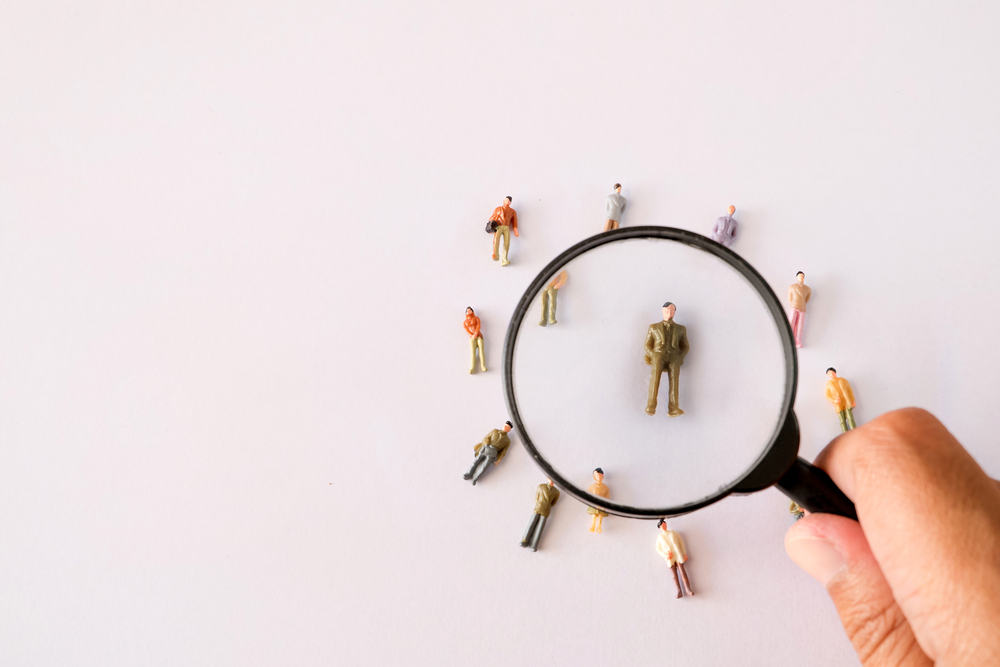 hand holding magnifying glass looking at figurines of people