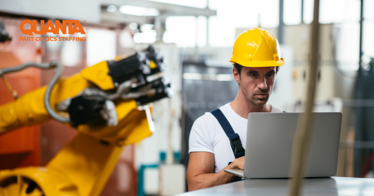 man in yellow hard hat looking at laptop with machinery in the background