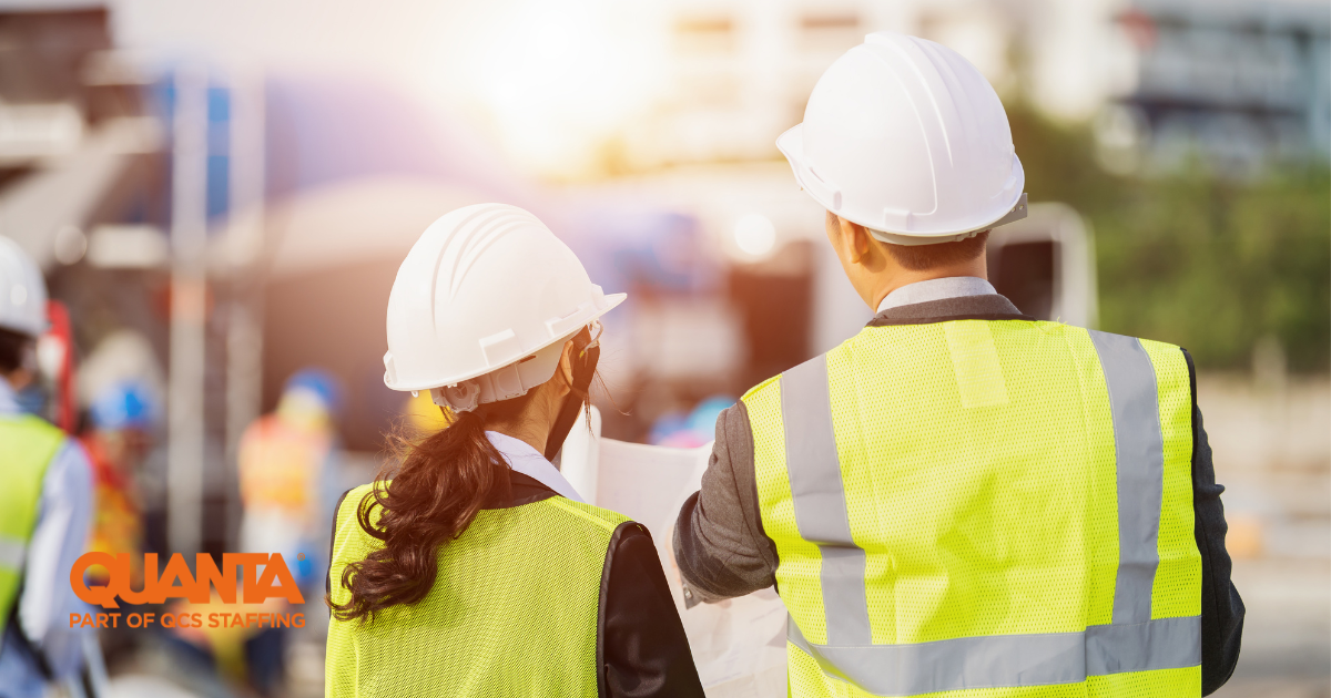 two people in hard hats and high visibility jackets looking at large rolled up sheets of paper