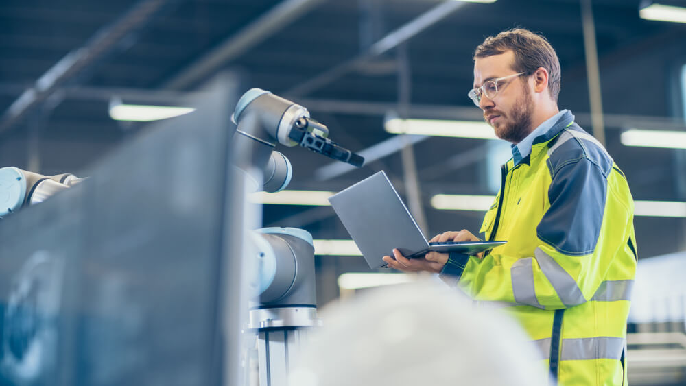 automation engineer Uses Laptop for Programming Robotic Arm