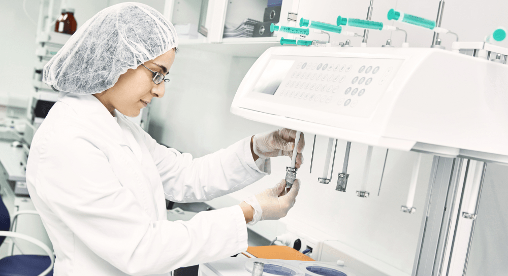 person in white lab coat and hair net using medical equipment