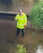 Curtis wearing a yellow high vis jacket standing in a stream under a bridge