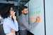 Project management jobs - man writing on post-it note with women looking at his notes 