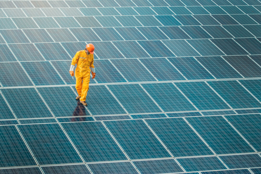 person in orange jumpsuit and hard hat checking equipment at solar farm