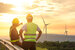 two people in hard hats and high visibility jackets looking at wind turbines in the distance