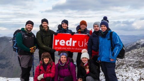 Image of a group of people dressed in winter gear on top of a mountain holding the redR banner