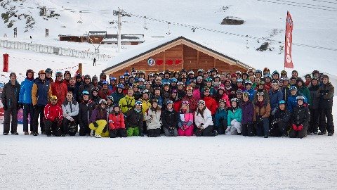 Image of 100 people dressed in vibrant ski clothing on snowy slopes