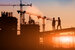 Silhouette of two civil engineers at sunset with cranes in the background