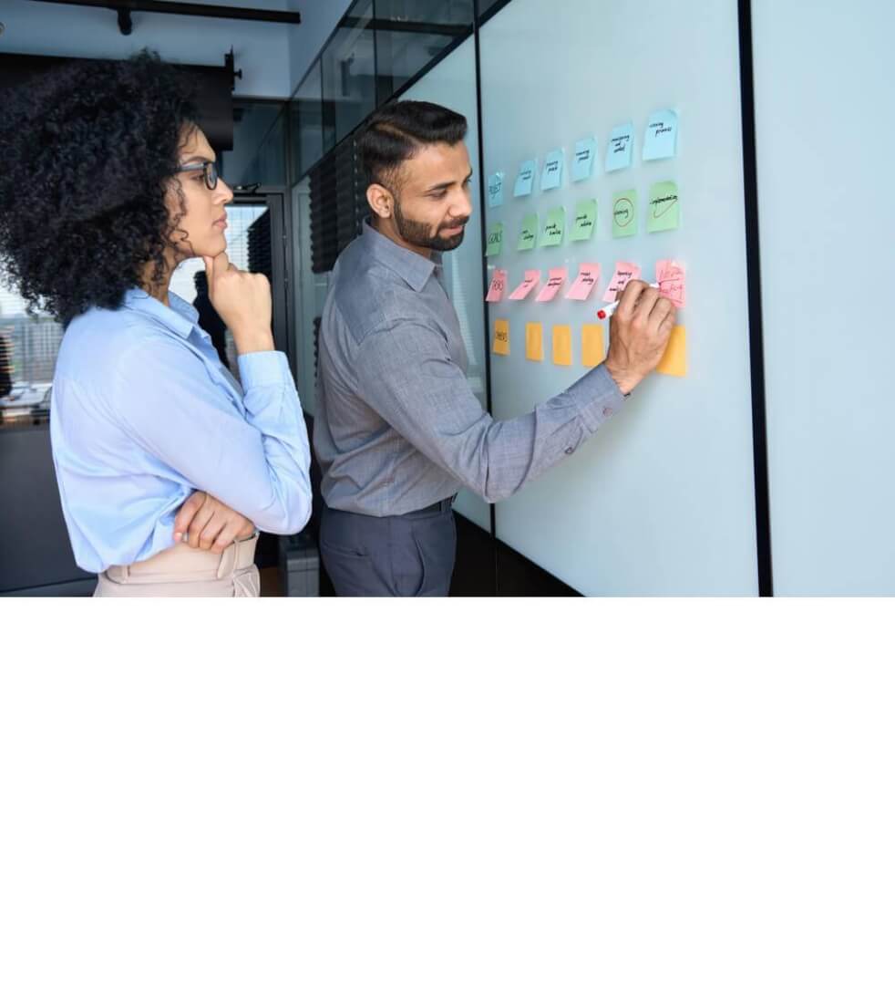 people standing at whiteboard writing on sticky notes