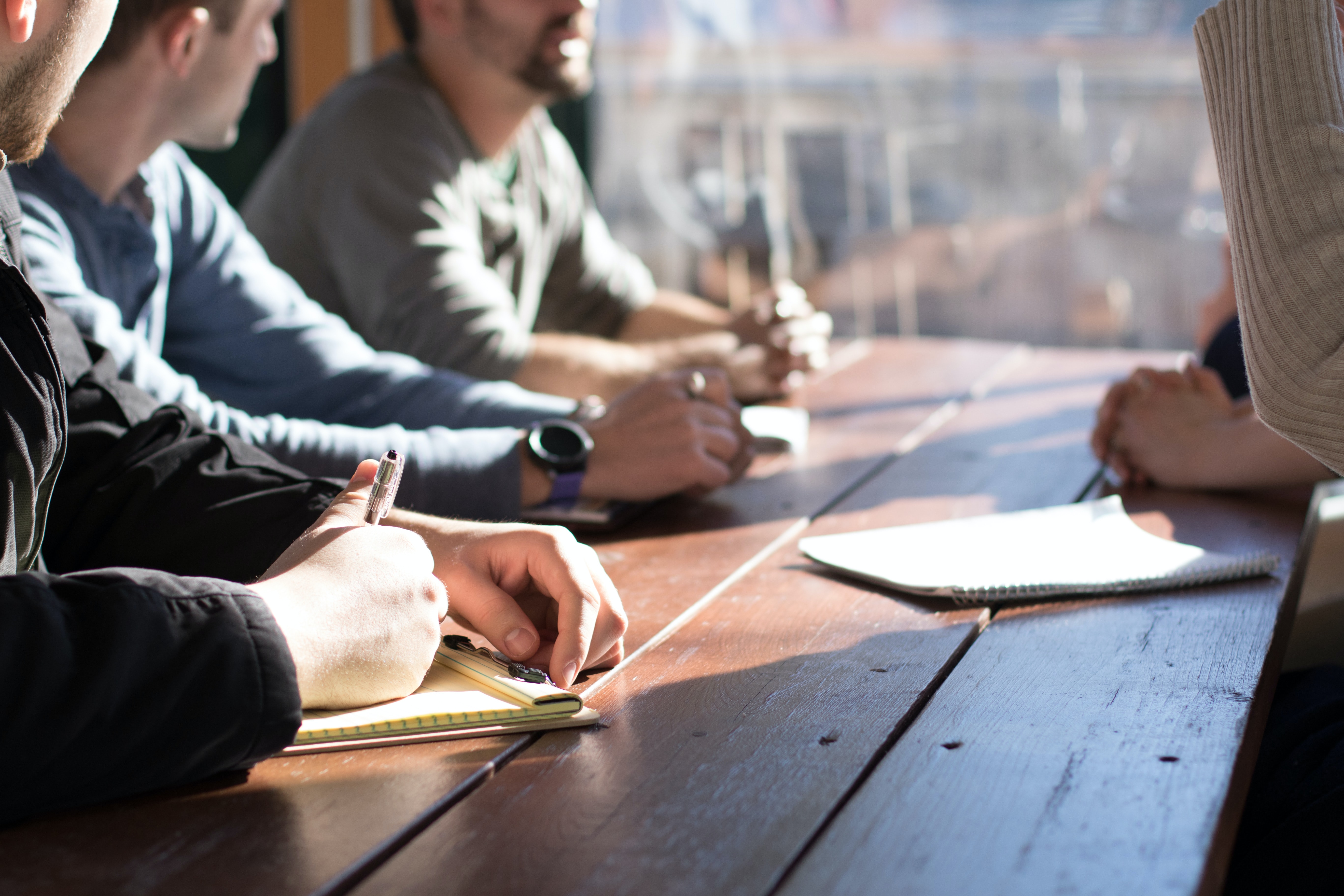 row of hands placed on a table with notepads and pens