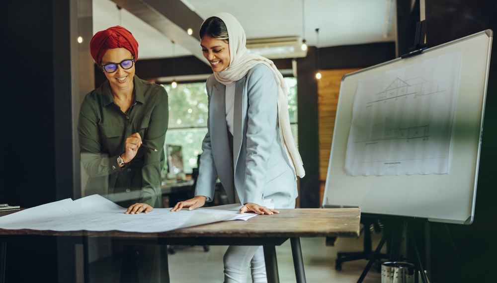 Two Middle Eastern female engineers collaborating on construction design in an office setting.