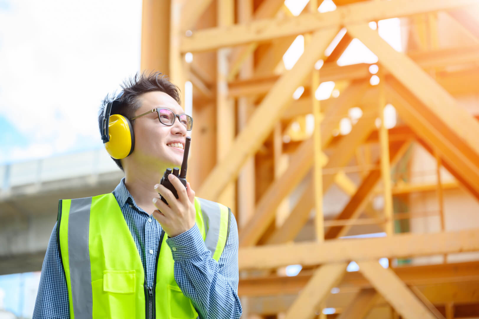 Young asian engineers are working on the construction site. Wear a yellow earmuff sound protection and uniform staff. Hand holding portable radio transceiver for communication