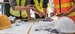 Three construction workers stood over a table which has plans, tools and hard hats on it