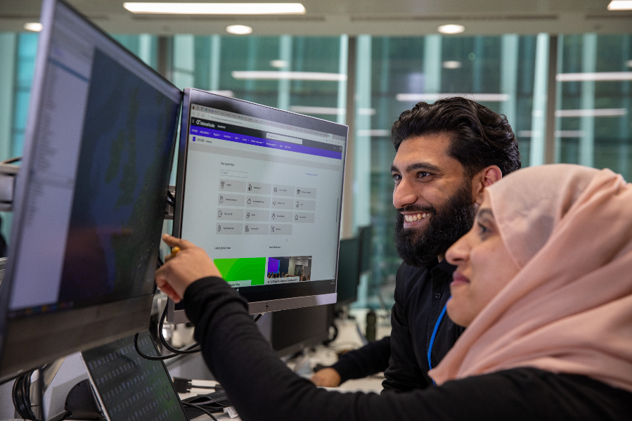 man and woman in headscarf smiling and pointing at screen in London nova office