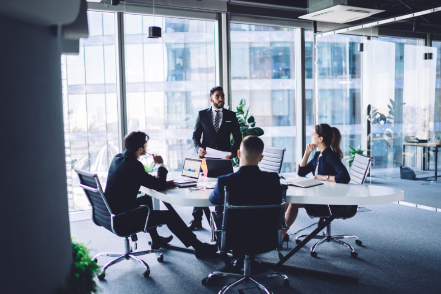 businessman making training conference meeting with male and female employees explaining statistic information from corporate report, group of experienced people discussing strategy teamwork