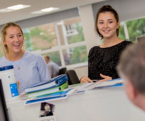 This is an image of colleagues in discussion over a work desk