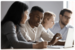 Four professionally dressed people sat at a table with a laptop.