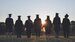 Silhouettes of graduates standing in a meadow with their back to the camera.