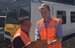 Two engineers in high vis jackets holding a clipboard standing in front of a train.