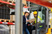 Forklift driver talking with health and safety manager in modern industrial factory.