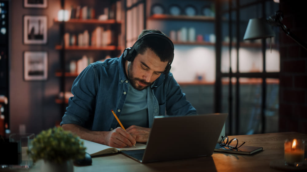 Man With Headphones Listening Music on Laptop while Sitting in Dim Living Room in the Evening, preparing for an interview in the oil and gas industry