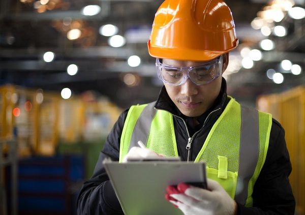 A man in a high vis jacket with an orange hardhat holding a clipboard.