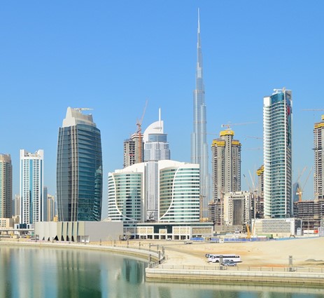 some skyscrapers on a beach in front of some water with a blue sky in the background