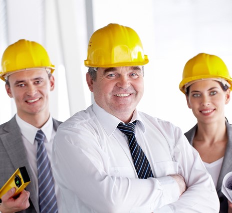 Three people in suits and yellow hardhats smiling at the camera