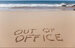 A picture of a beach, with out of office written in the sand