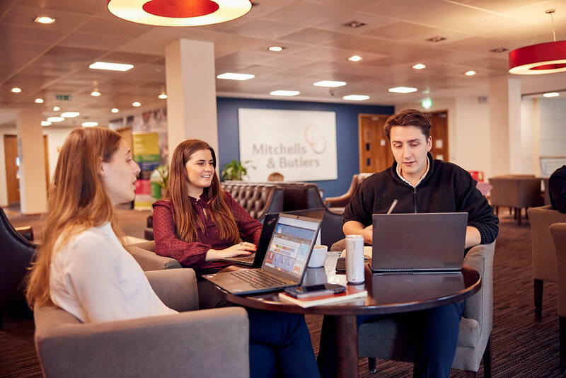 three people sitting in circle while talking and looking at laptops