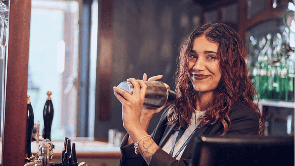 assistant manager smiling whilst shaking a cocktail shaker