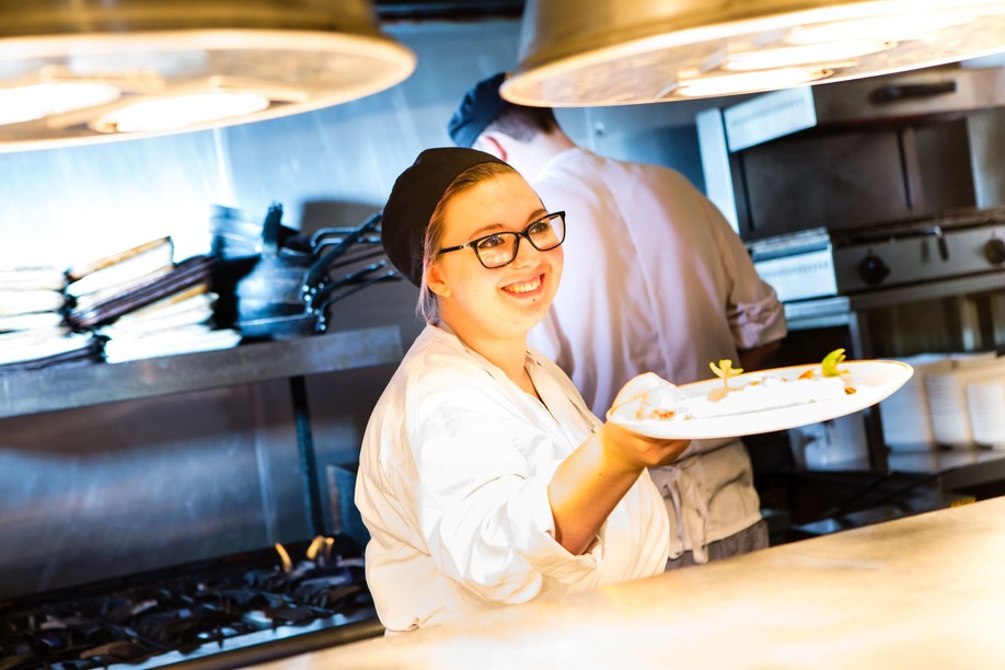 Smiling female chef holding plate under heat lamp in a restaurant job
