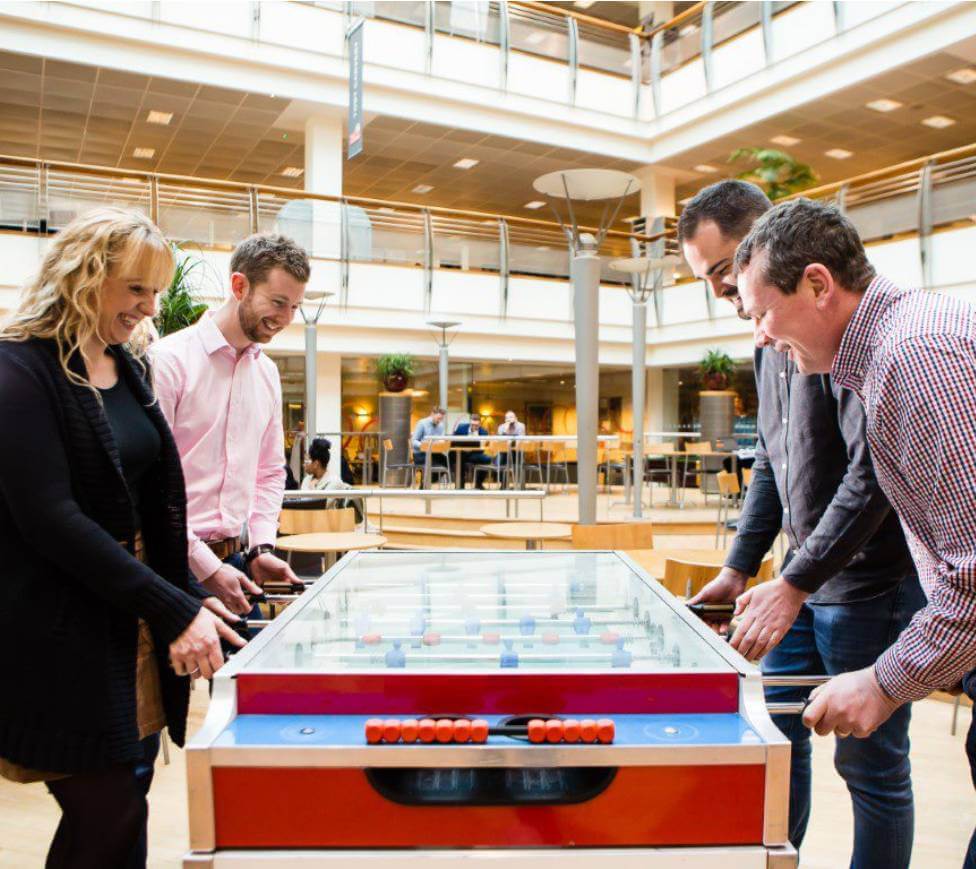 four employees in a large office, enjoying a game of table football 