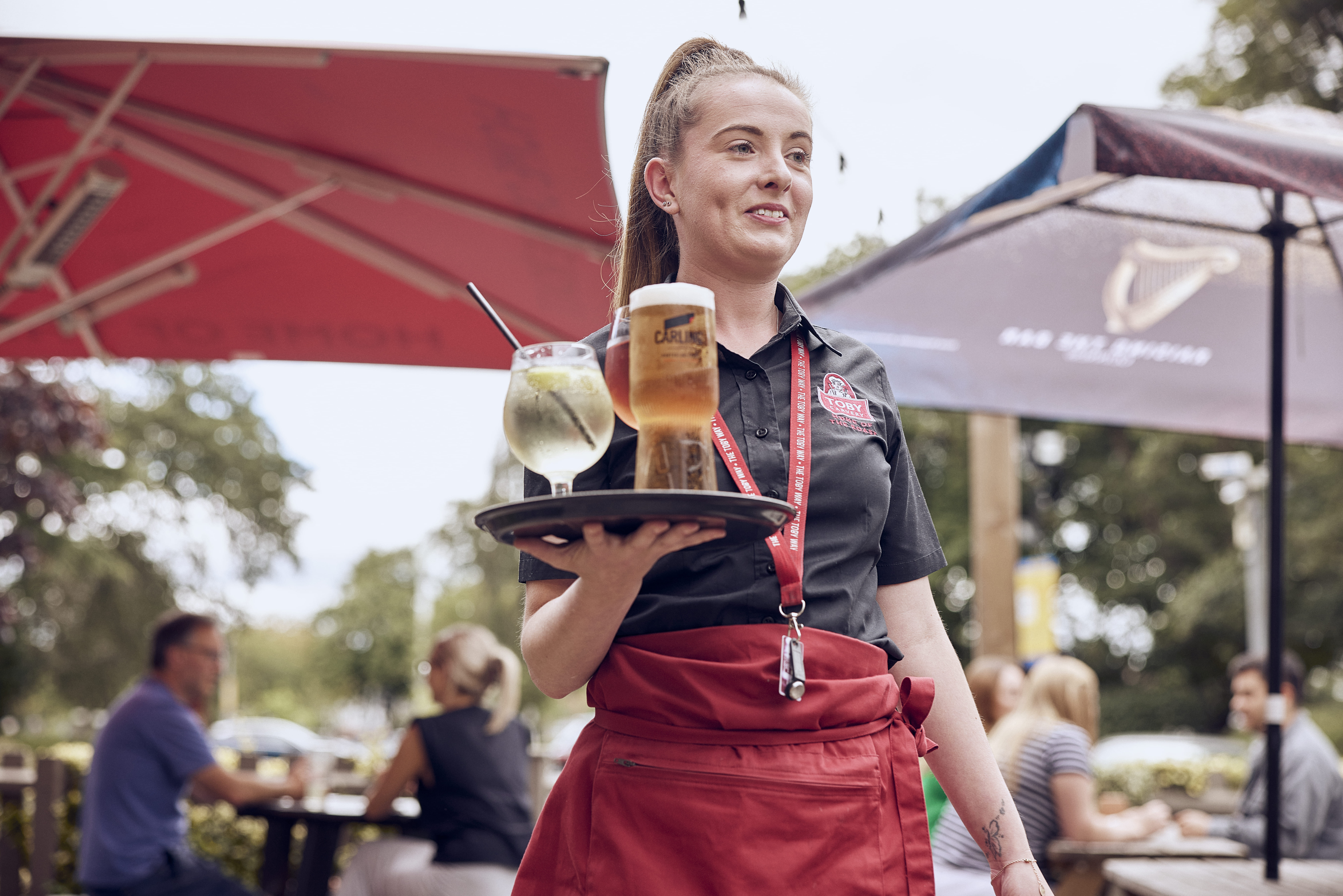 bar staff smiling holding a tray with drinks in summer beer garden 