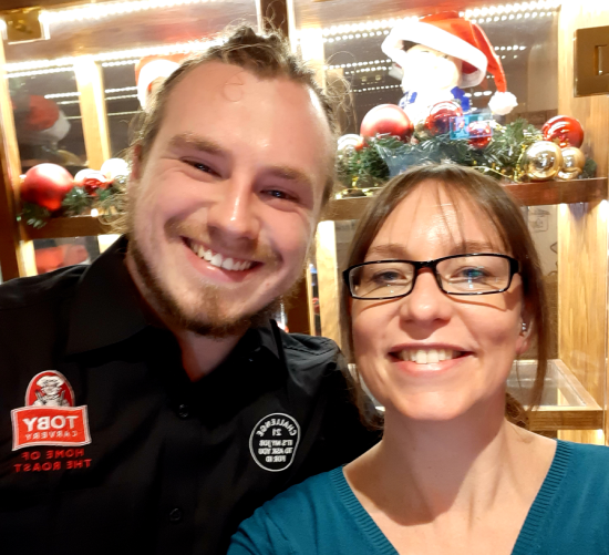 Assistant manager seating two customers smiling and holding menu 