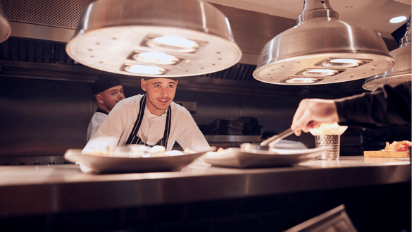 Chef apprentice looks at the food on the kitchen pass. 