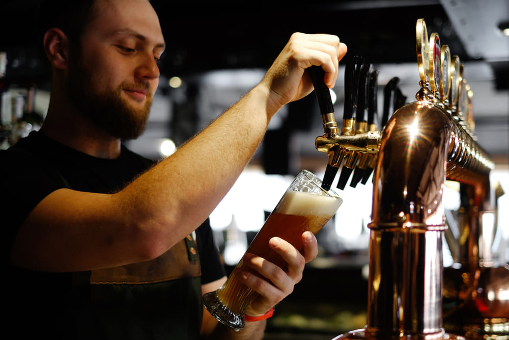 smiling bearded man the bartender pours a draft beer, enjoying part time Christmas job