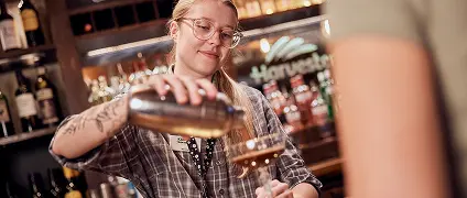A bartender pouring a cocktail into a glass