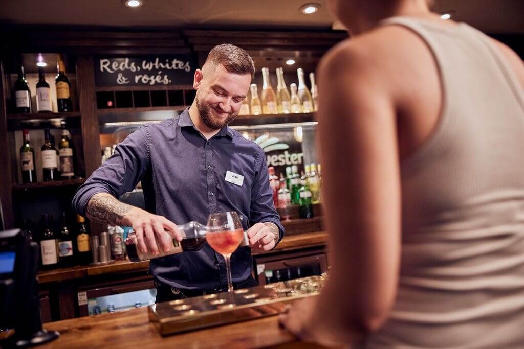 image of bartender pouring a drink for guest and smiling 