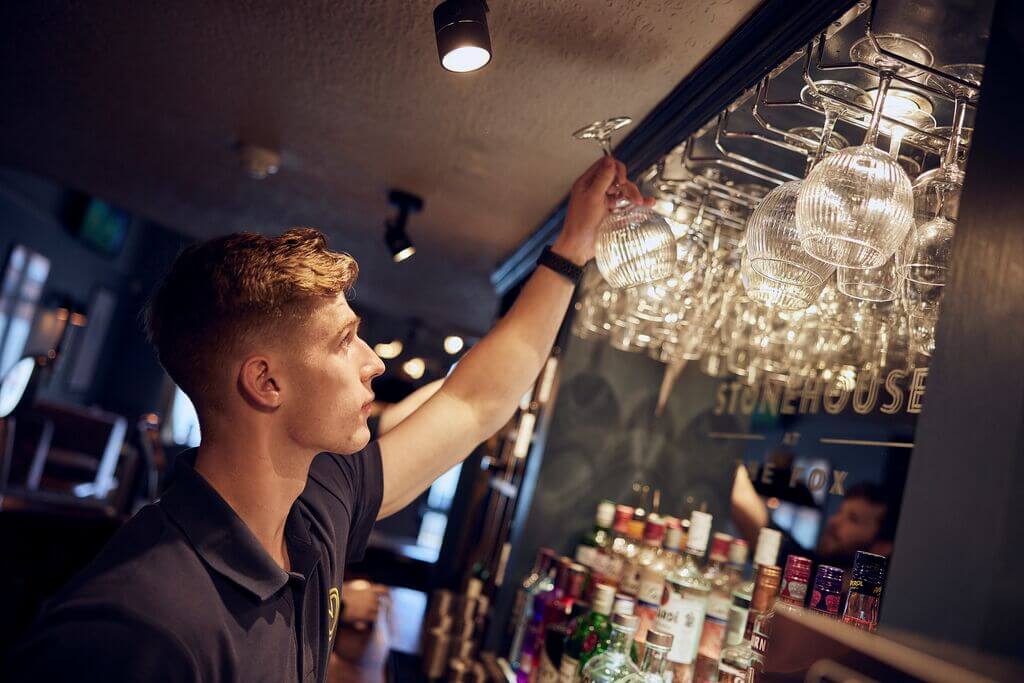parttime bar staff hanging up glasses