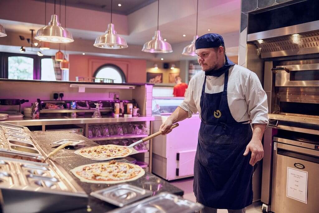 chef making pizza and putting it into an oven 