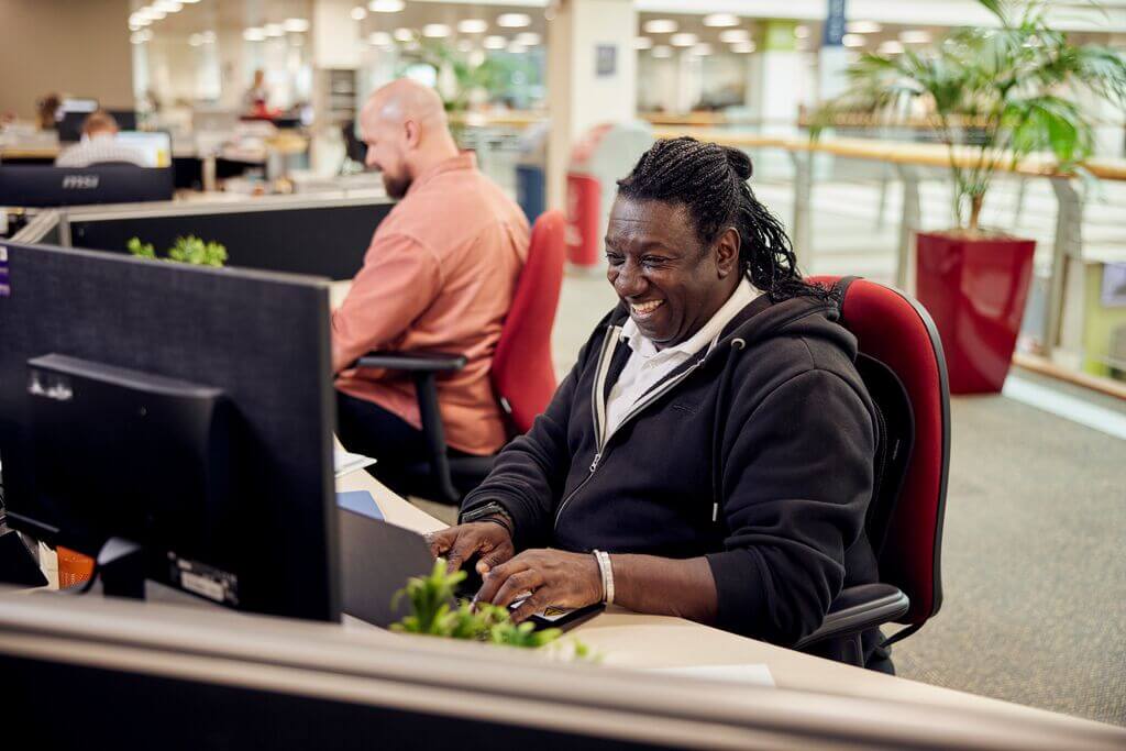 Man smiling at computer in a head office job at M&B 