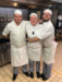 three chefs standing in a kitchen smiling and hugging
