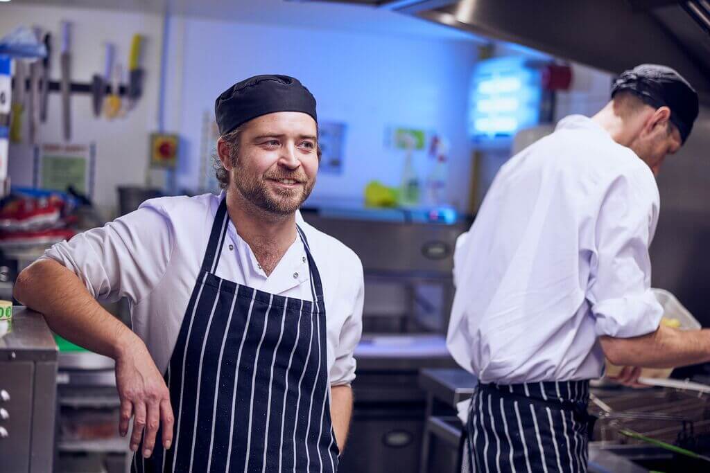 image of kitchen team cooking in the kitchen wearing aprons and hats