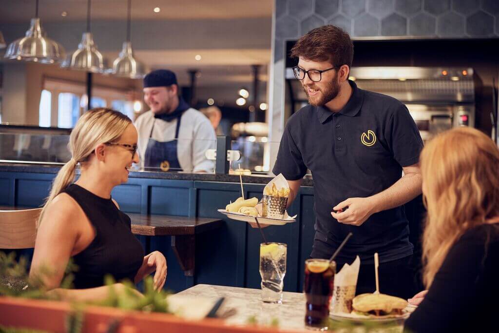 wait staff serving food to guests at M&B with a smile