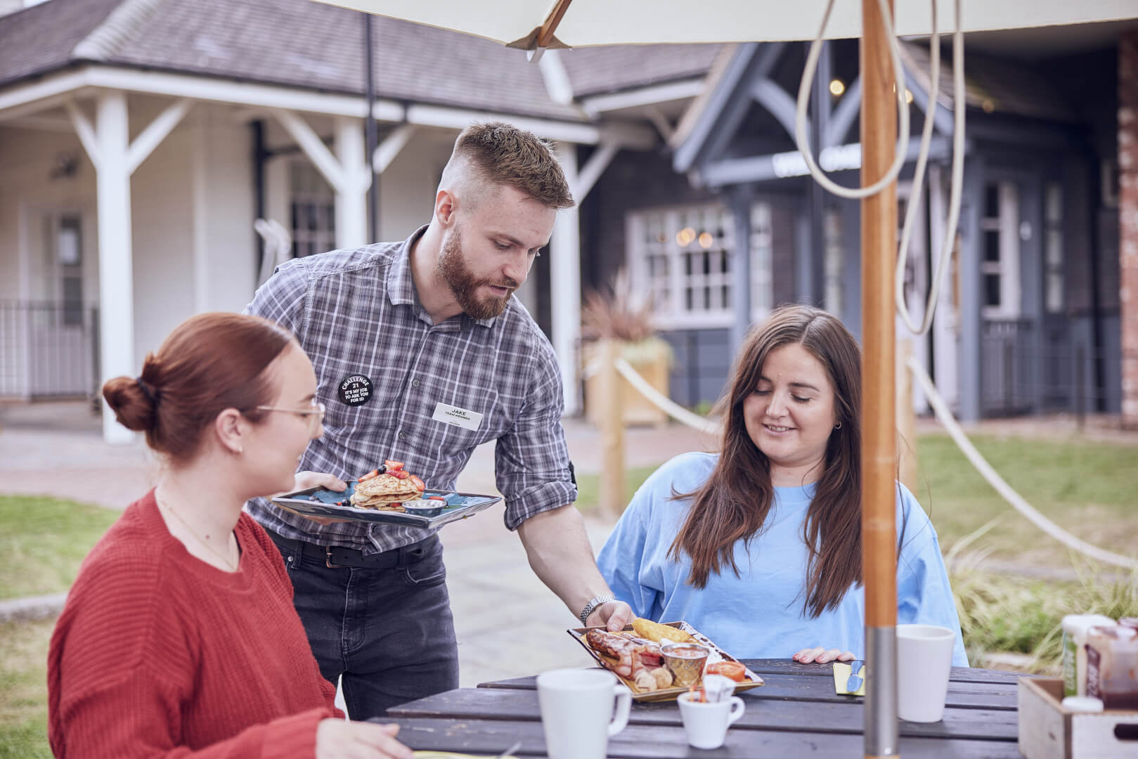 image of a man serving food to guests sitting outside 