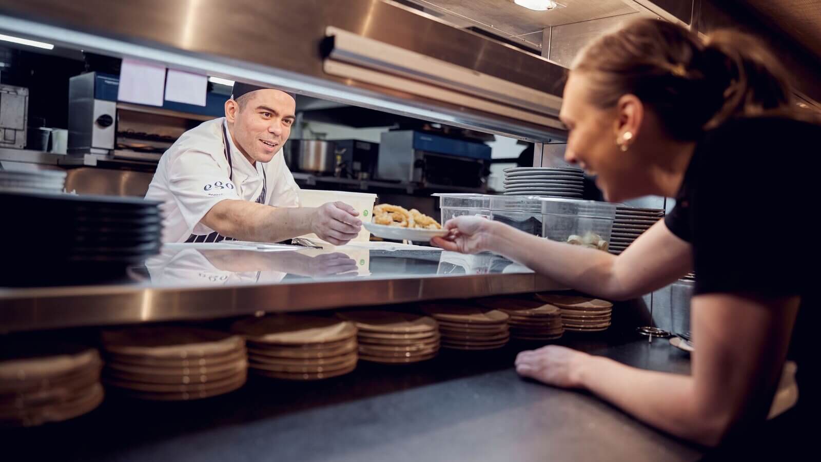 image of ego employees in the kitchen passing plate of food 